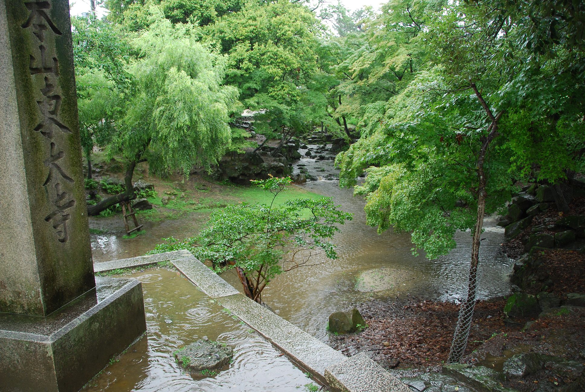雨中的东大寺附近庭园溪流、树木与刻字石柱。
