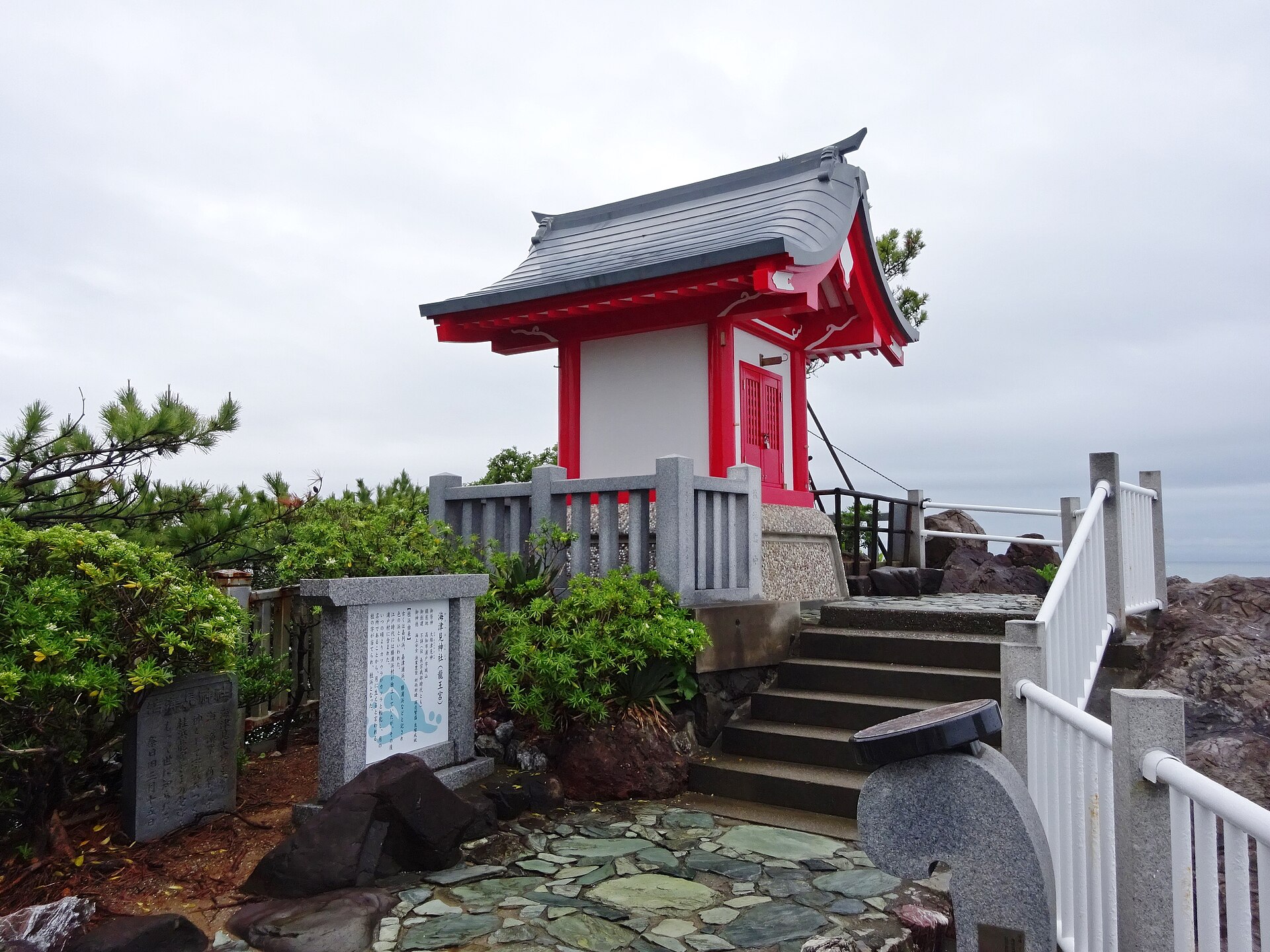 桂浜岬上的海津见神社（龙王宫），朱红色小社殿围着石栏杆，前有石阶与松树，天色阴沉。