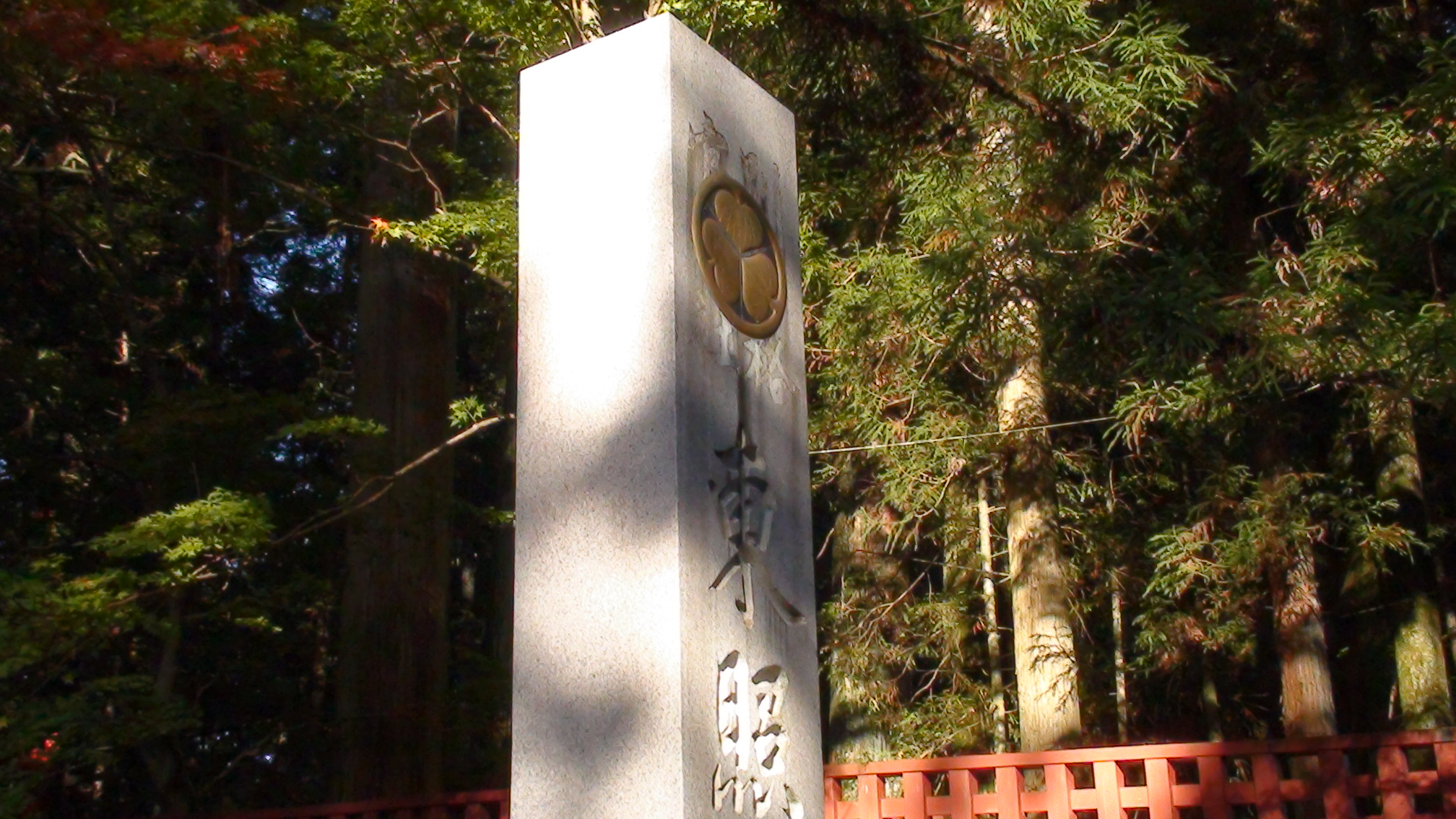 树林中带德川家纹的日光东照宫石柱与红色栏杆。