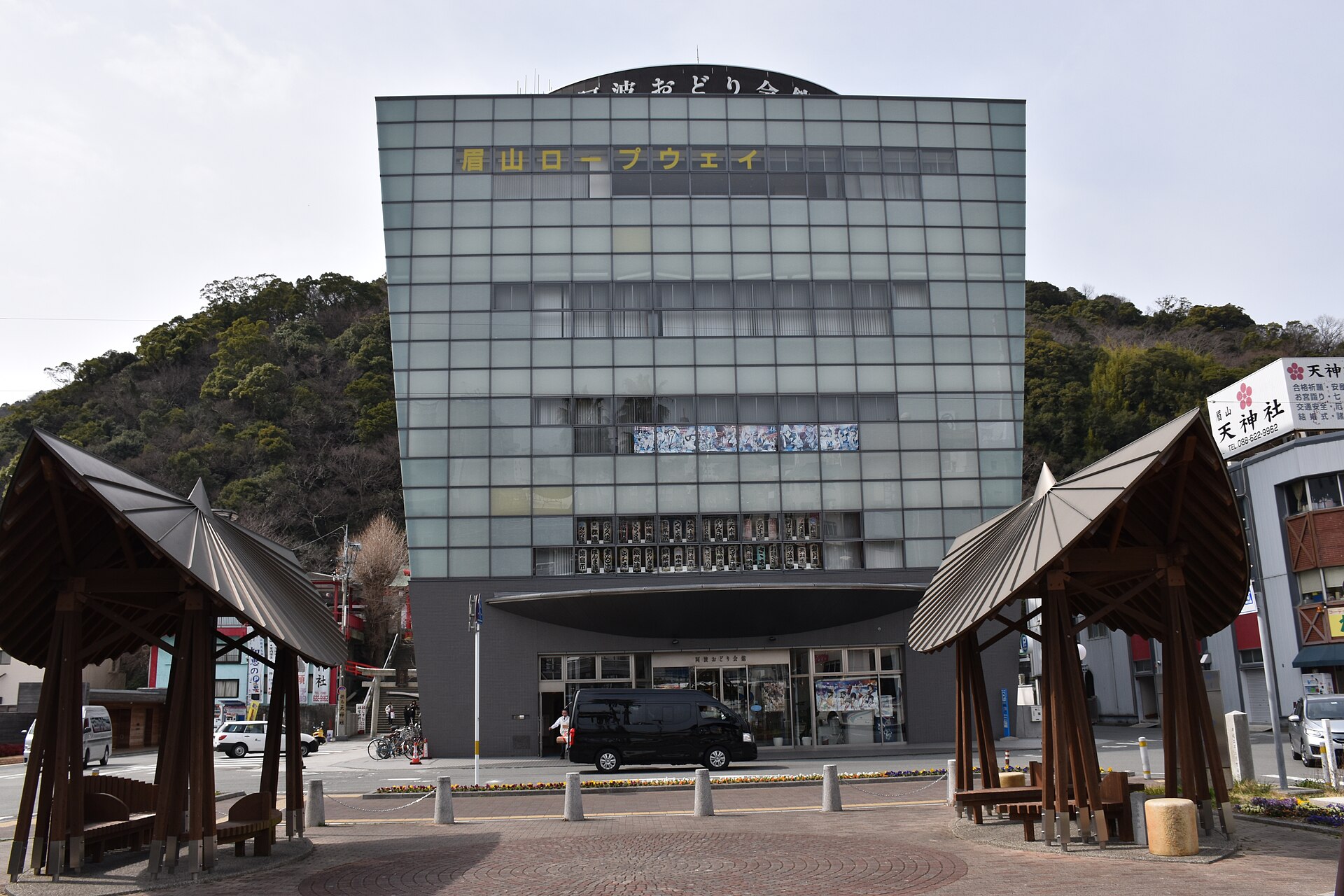 德岛阿波舞会馆的玻璃幕墙外观，楼后是眉山的树林山坡。