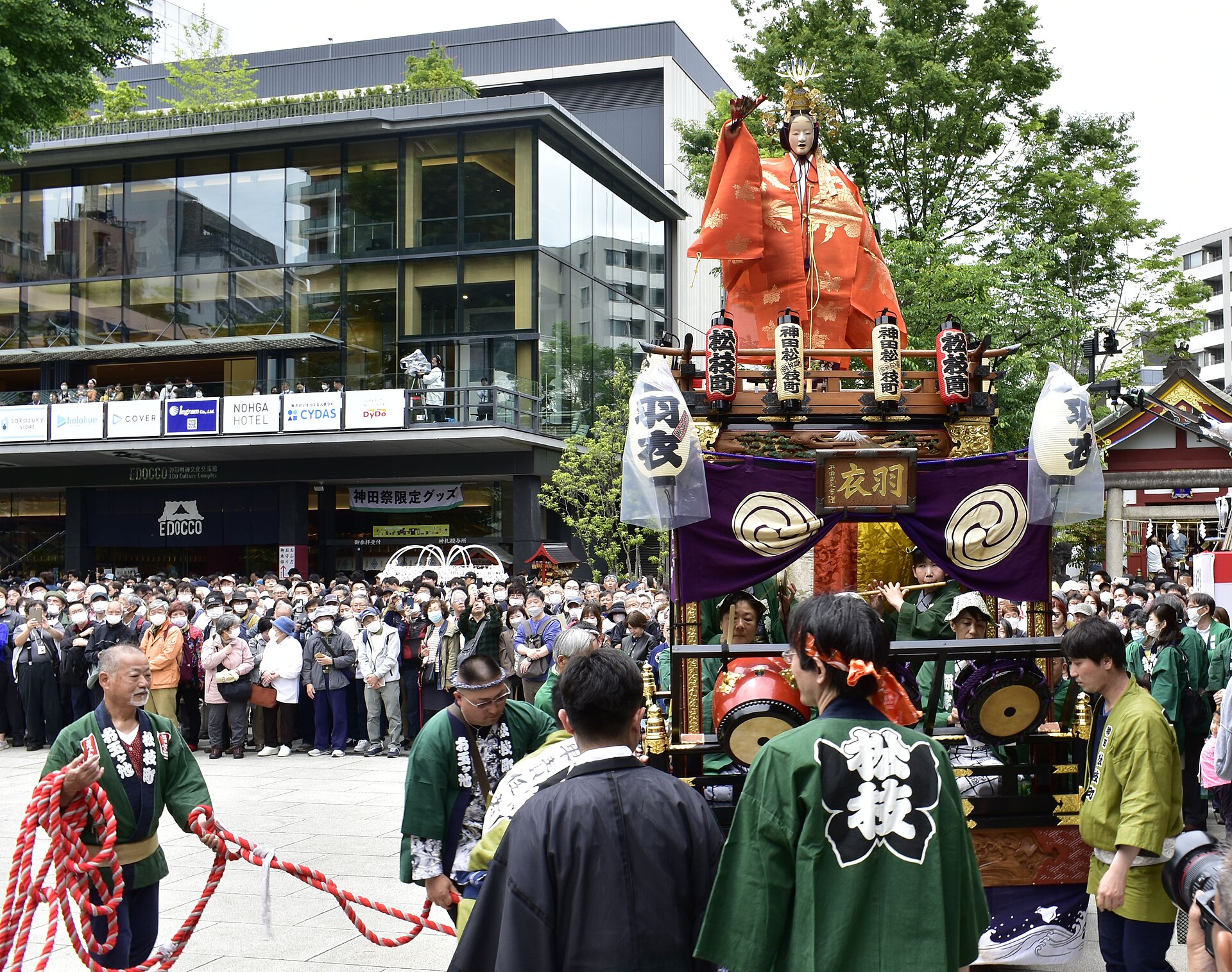 神田祭上，身穿绿色法被的人们用红白粗绳拉动「羽衣」山车，车上乐手吹笛击鼓，顶端立着天女人偶。