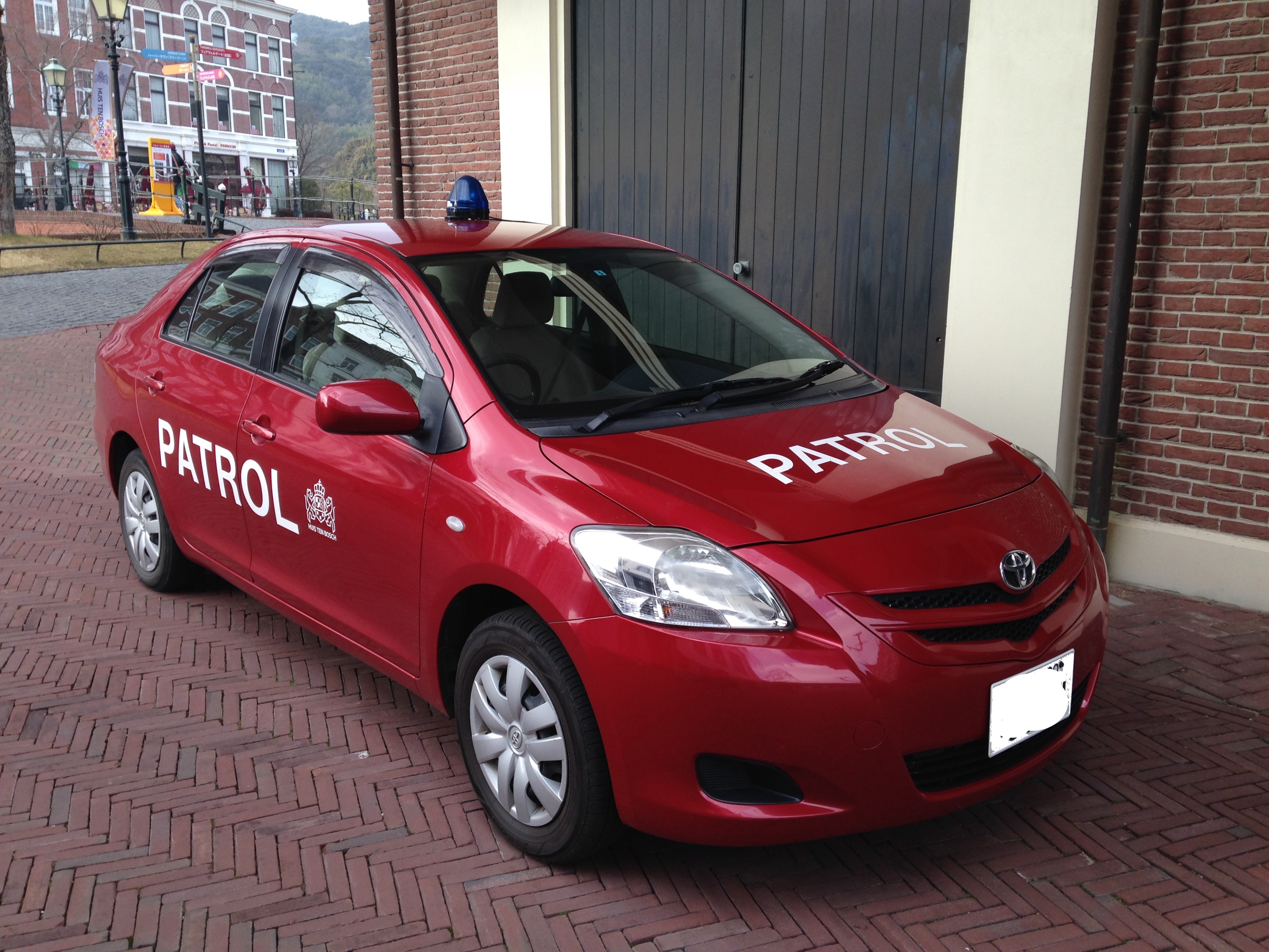豪斯登堡园内，一辆车顶装着蓝色警灯、车身写有 PATROL 的红色巡逻轿车停在红砖路面上。